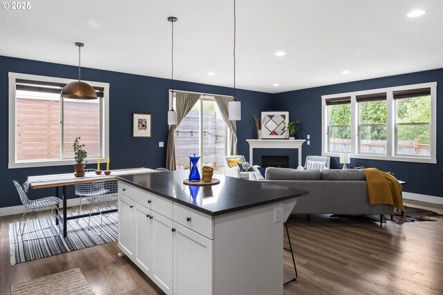 kitchen featuring white cabinets, dark countertops, a fireplace, dark wood-type flooring, and a kitchen island