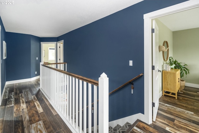 corridor featuring baseboards, wood finished floors, and an upstairs landing
