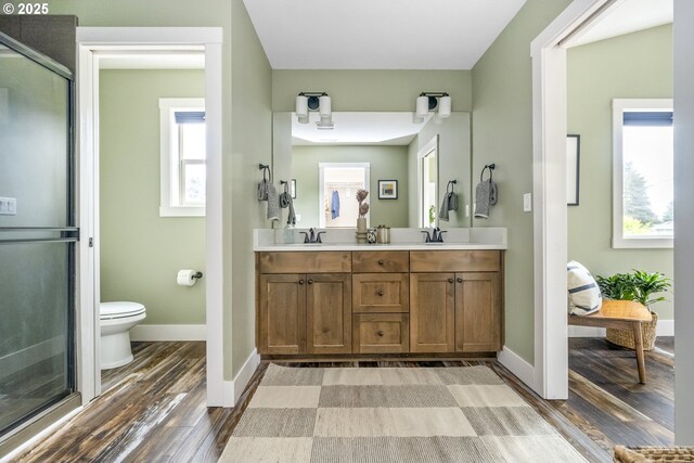 bathroom with double vanity, a stall shower, toilet, and wood finished floors