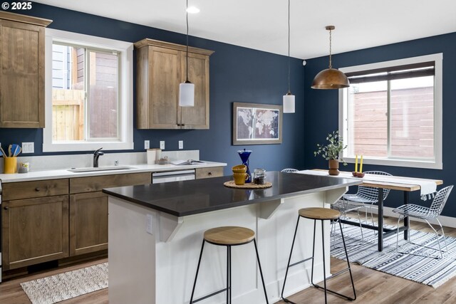 kitchen with a sink, wood finished floors, hanging light fixtures, and a kitchen bar