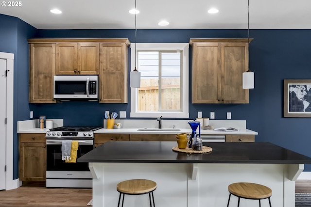 kitchen with wood finished floors, dark countertops, a breakfast bar, a sink, and appliances with stainless steel finishes
