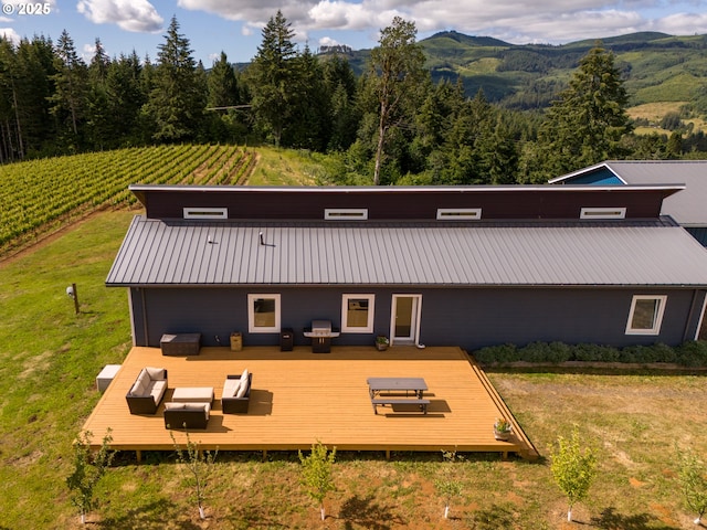 rear view of property with an outdoor hangout area, a deck with mountain view, a view of trees, a lawn, and metal roof