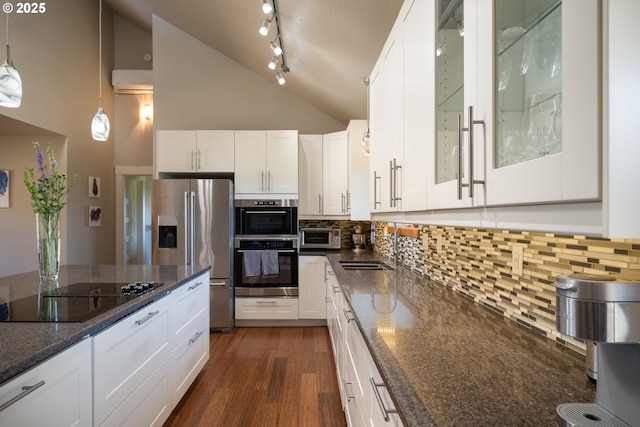 kitchen with dark stone counters, appliances with stainless steel finishes, white cabinets, and high vaulted ceiling