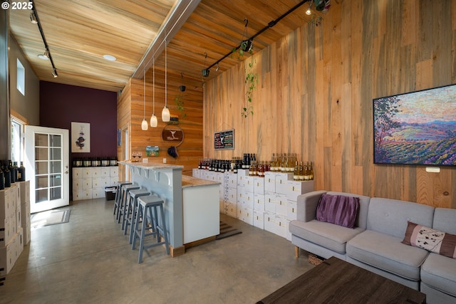 interior space with concrete flooring, a high ceiling, wooden walls, wooden ceiling, and hanging light fixtures