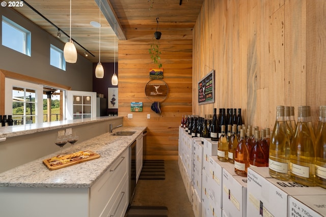 interior space featuring a towering ceiling, wooden walls, rail lighting, a sink, and hanging light fixtures