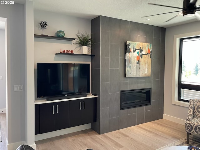 113 NW Willard St, Stevenson, WA 98648 - living room featuring ceiling fan, light wood-type flooring, baseboards, a tile fireplace, and a textured ceiling