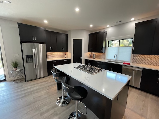 kitchen with a breakfast bar, light countertops, dark cabinets, a sink, and appliances with stainless steel finishes