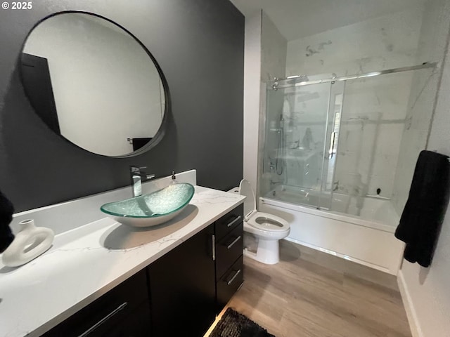 full bath with vanity, shower / bath combination with glass door, wood finished floors, and toilet