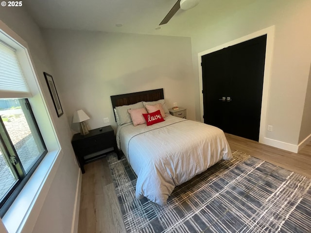 bedroom featuring baseboards, ceiling fan, multiple windows, and wood finished floors