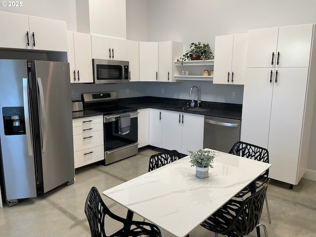 kitchen featuring concrete flooring, open shelves, appliances with stainless steel finishes, a sink, and a towering ceiling