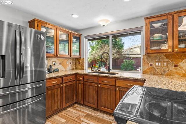 kitchen with stainless steel fridge with ice dispenser, light wood-type flooring, light stone countertops, and a sink