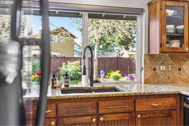 kitchen featuring a sink, tasteful backsplash, brown cabinetry, and glass insert cabinets