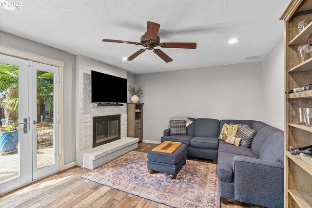 living room featuring visible vents, a brick fireplace, baseboards, wood finished floors, and a ceiling fan