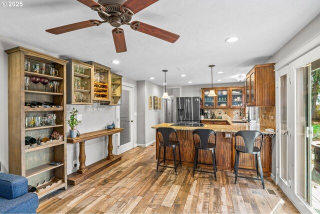 kitchen with a sink, light wood finished floors, light stone countertops, stainless steel fridge, and a peninsula