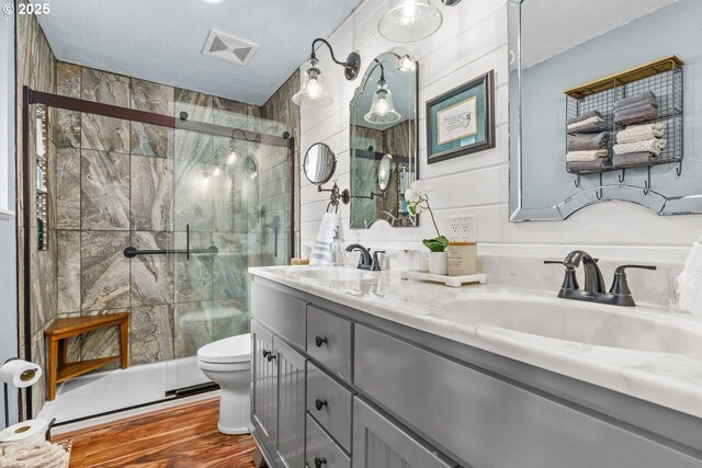 bathroom with a shower stall, double vanity, wood finished floors, and a sink
