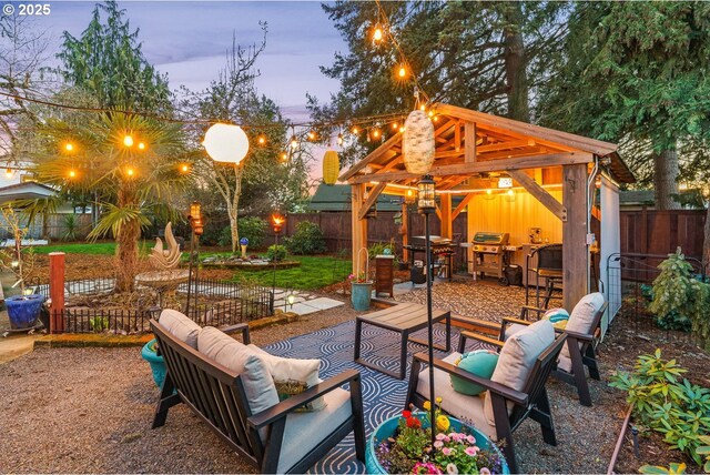 patio terrace at dusk with outdoor dry bar, an outdoor hangout area, a grill, a fenced backyard, and a gazebo