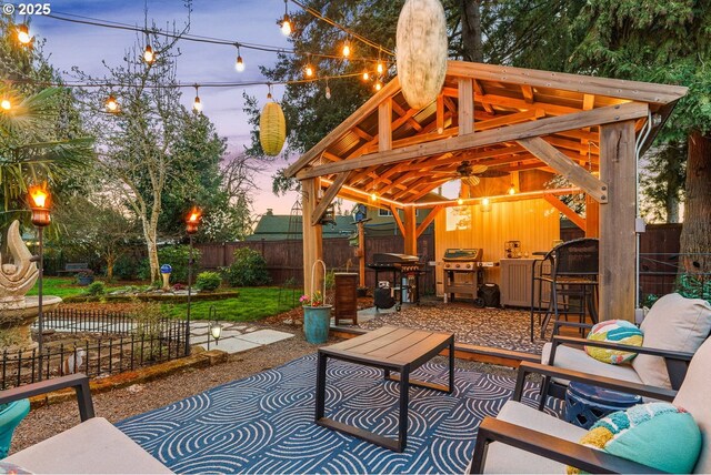 patio terrace at dusk featuring a fenced backyard, outdoor dry bar, and a grill