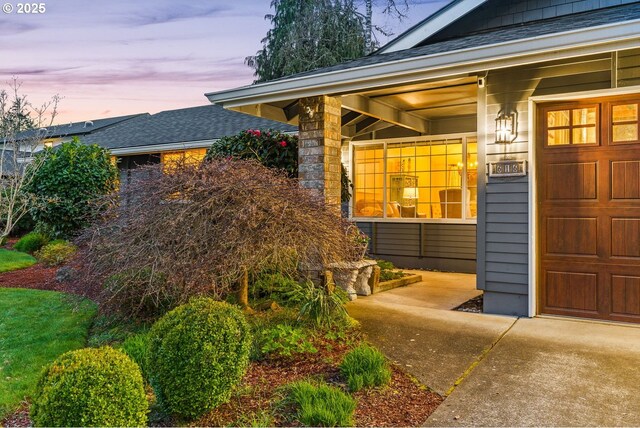exterior entry at dusk featuring a garage and roof with shingles