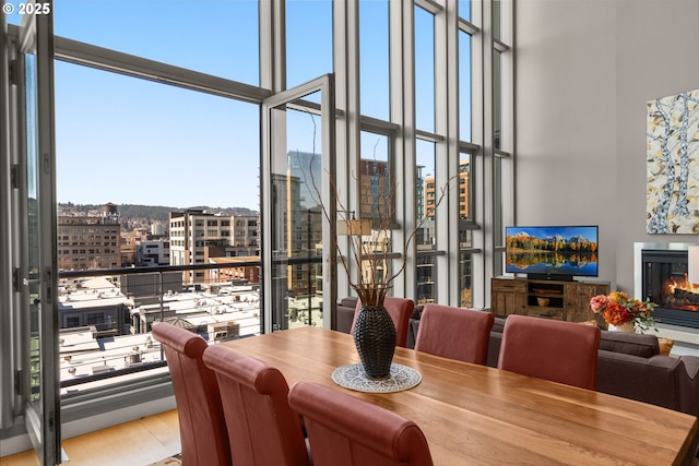 dining space with a city view, wood finished floors, a towering ceiling, floor to ceiling windows, and a glass covered fireplace