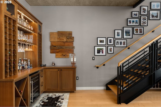 wine cellar with light wood-style floors, wine cooler, baseboards, and a dry bar