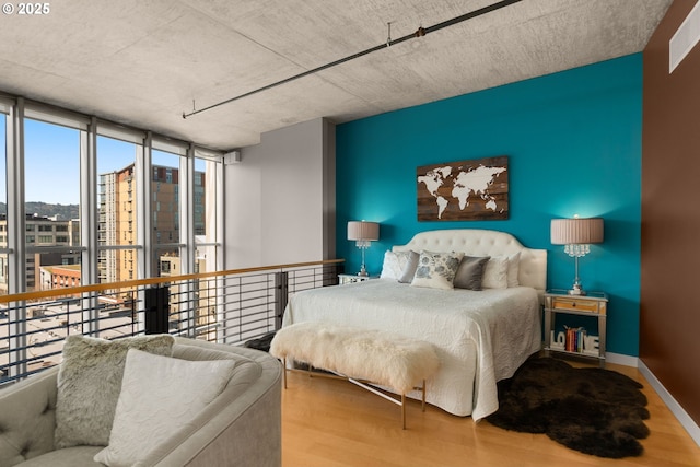 bedroom featuring an accent wall, floor to ceiling windows, baseboards, and wood finished floors