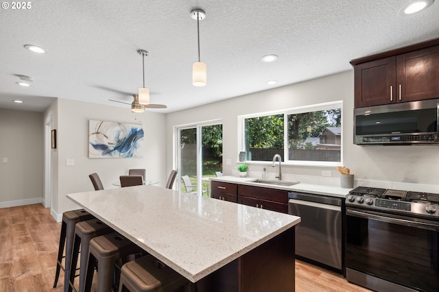40 SW 150th Ave, Beaverton, OR 97006 - kitchen with appliances with stainless steel finishes, a kitchen island, dark brown cabinetry, hanging light fixtures, and light stone counters