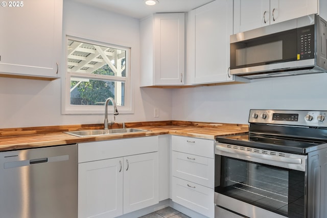 kitchen with butcher block counters, sink, white cabinetry, light tile patterned floors, and appliances with stainless steel finishes