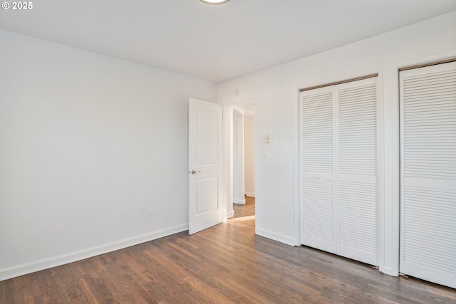 unfurnished bedroom with dark hardwood / wood-style flooring and multiple closets