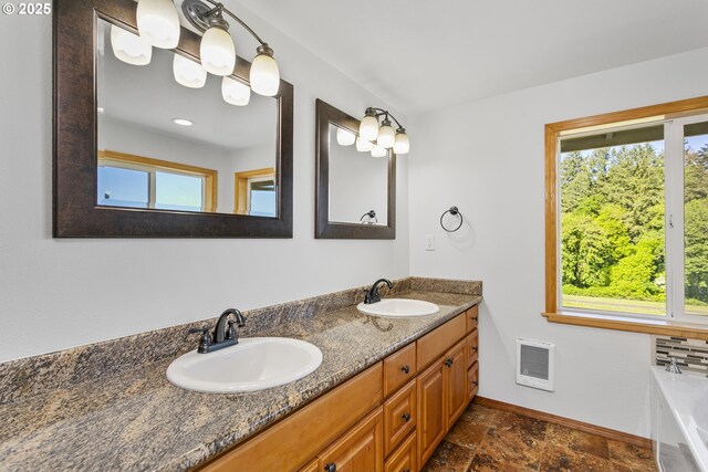 full bathroom featuring baseboards, double vanity, a tub to relax in, and stone finish floors