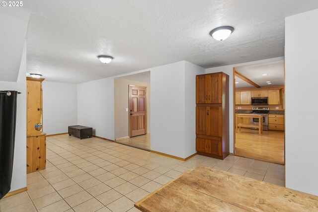 interior space featuring stainless steel appliances, light tile patterned floors, baseboards, and a textured ceiling