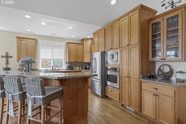 kitchen featuring light wood-type flooring, appliances with stainless steel finishes, a kitchen breakfast bar, dark stone counters, and decorative backsplash