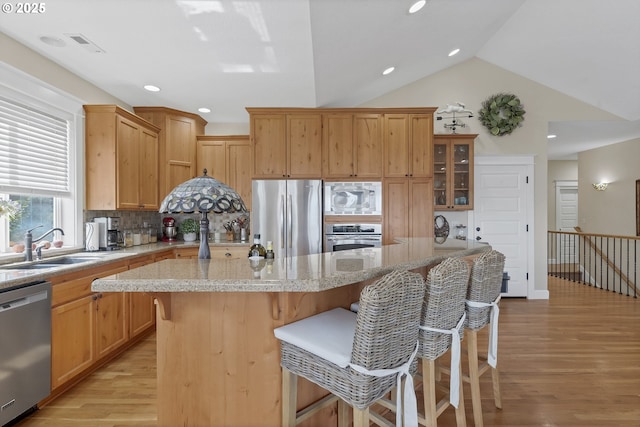 kitchen with a kitchen island, a breakfast bar, light stone counters, stainless steel appliances, and light hardwood / wood-style flooring