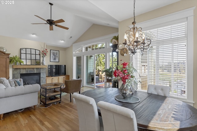 dining room featuring high vaulted ceiling, ceiling fan with notable chandelier, a fireplace, and light hardwood / wood-style floors