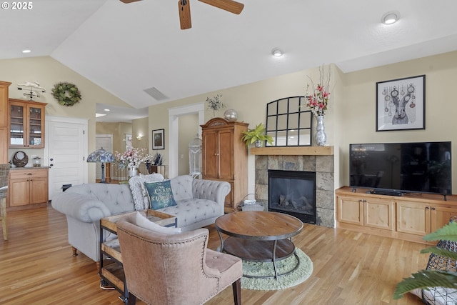 living room with ceiling fan, lofted ceiling, a fireplace, and light wood-type flooring