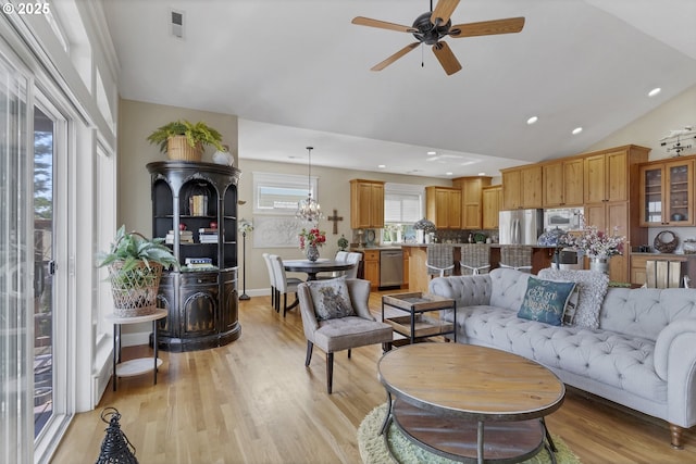 living room with vaulted ceiling, a wood stove, ceiling fan, and light wood-type flooring