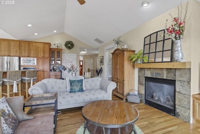 living room featuring ceiling fan, lofted ceiling, a fireplace, and light wood-type flooring