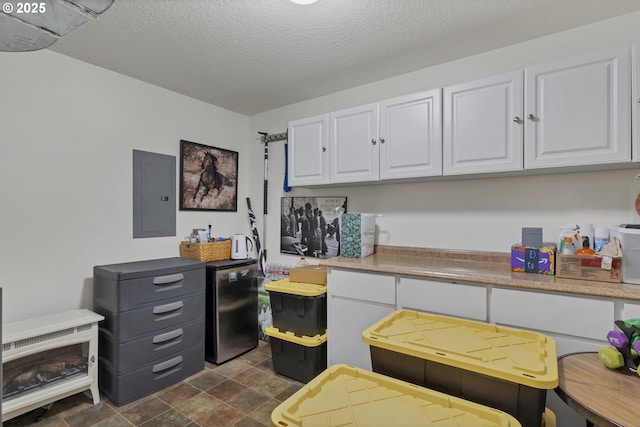 kitchen featuring stainless steel fridge, white cabinets, a textured ceiling, and electric panel