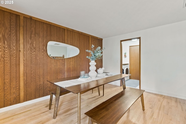 dining area featuring light wood-style floors, wood walls, baseboards, and independent washer and dryer
