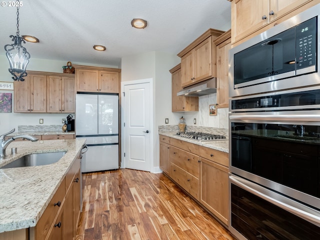 kitchen featuring a sink, light wood-style floors, light stone counters, under cabinet range hood, and appliances with stainless steel finishes
