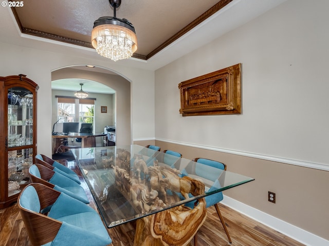 dining area featuring a tray ceiling, arched walkways, baseboards, a chandelier, and wood finished floors