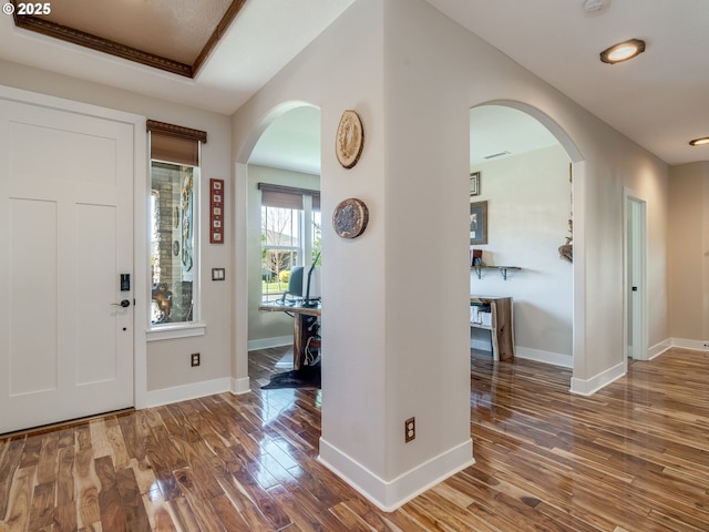 foyer featuring baseboards, wood finished floors, and arched walkways
