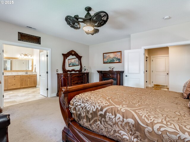 bedroom with visible vents, light carpet, a sink, baseboards, and ensuite bathroom