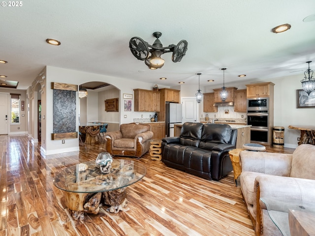 living area featuring arched walkways, light wood finished floors, and recessed lighting