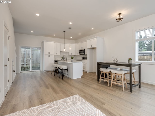 kitchen with stainless steel microwave, a kitchen island with sink, white cabinets, and tasteful backsplash