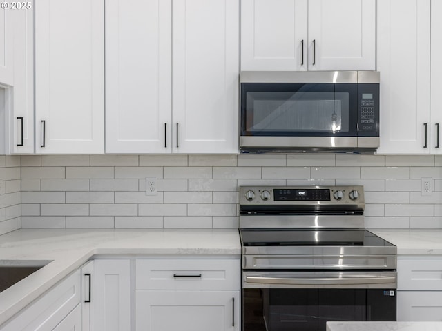 kitchen with light stone counters, white cabinets, stainless steel appliances, and tasteful backsplash