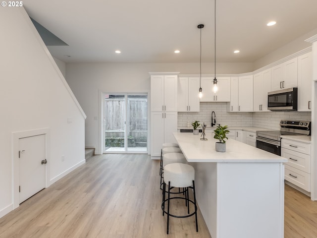kitchen with a breakfast bar area, light wood-type flooring, white cabinets, appliances with stainless steel finishes, and backsplash