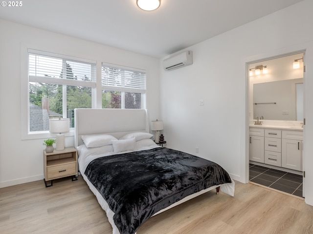 bedroom with a sink, baseboards, an AC wall unit, light wood finished floors, and ensuite bathroom