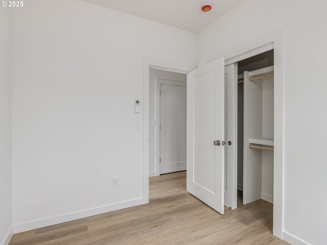 unfurnished bedroom with a closet, baseboards, and light wood-type flooring
