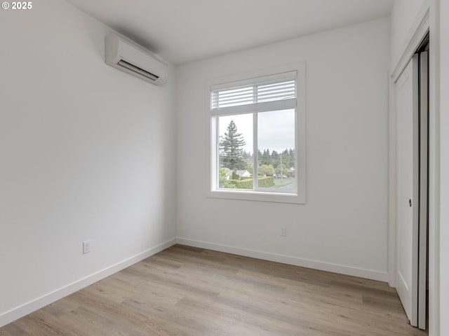 unfurnished bedroom with baseboards, a wall mounted AC, a closet, and light wood-style flooring