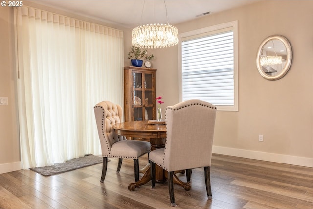 dining room featuring a chandelier, wood finished floors, visible vents, and baseboards